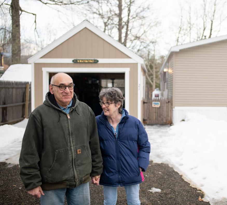 An elderly couple share a smile while standing in front of their home in the resident-owned Mountainside Mobile Home Community in Camden, Maine.