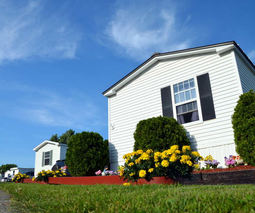 A few mobile homes with lush landscaping under a bright blue sky at Sunset Terrace in Rockland, Maine.