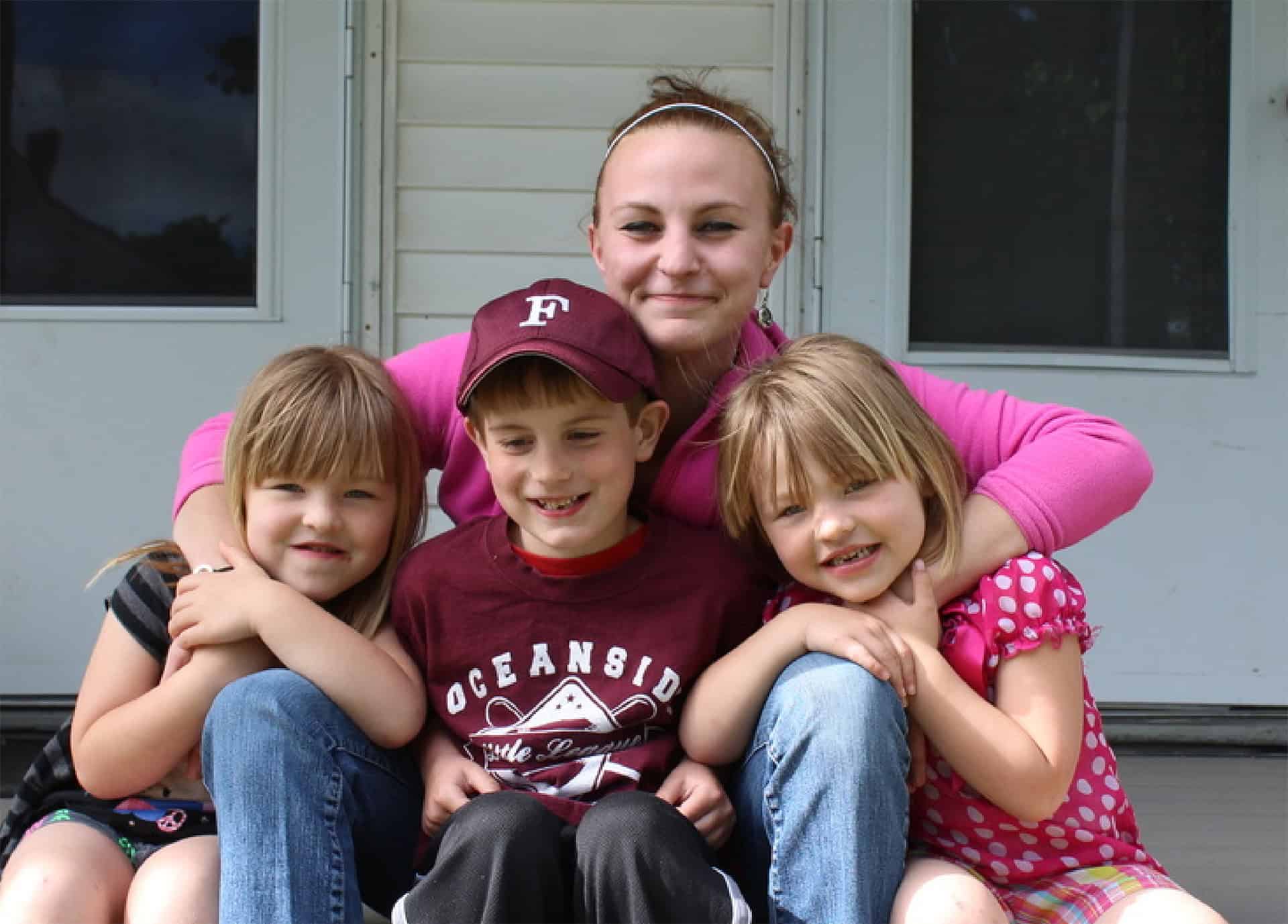 Smiling woman with three children outdoors, promoting community and family support.