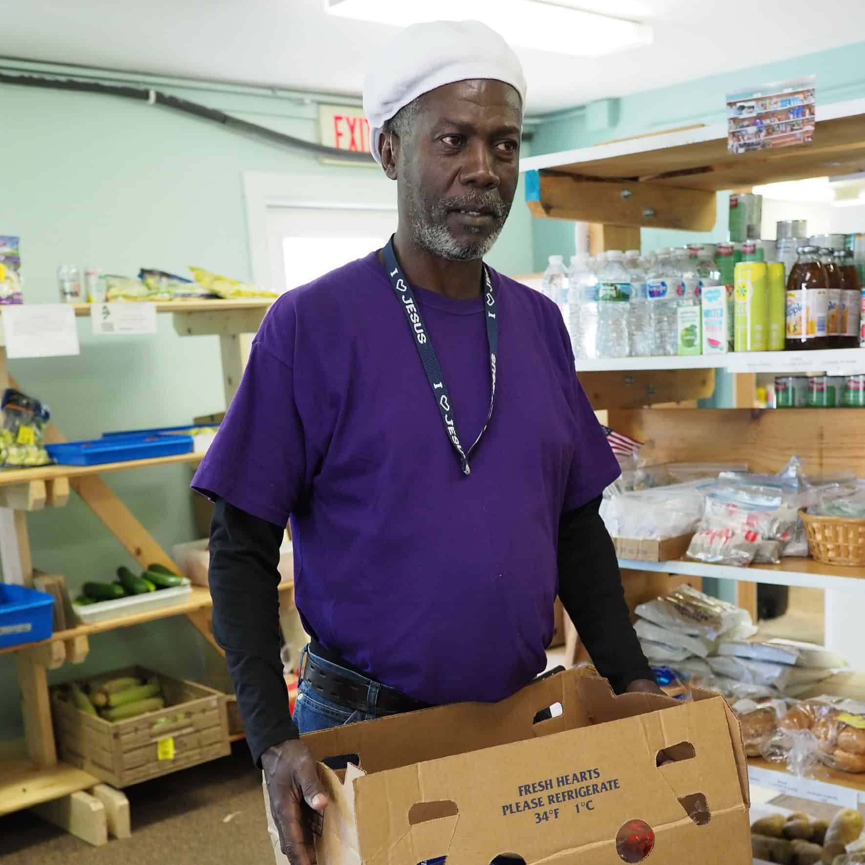 Man in purple T-shirt volunteering at food pantry and carrying a box of groceries