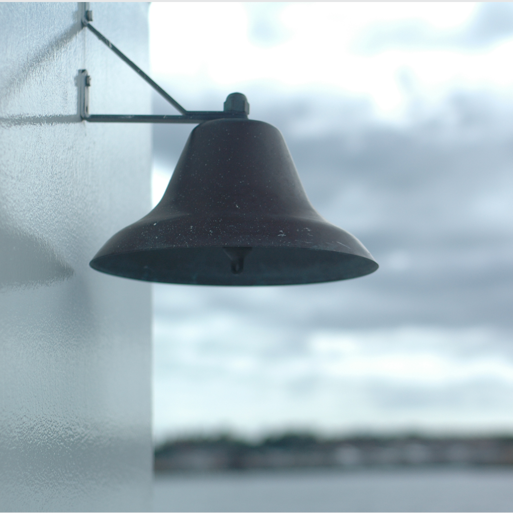 Small weathered bell on a building on a Maine island, with blurred view of ocean water