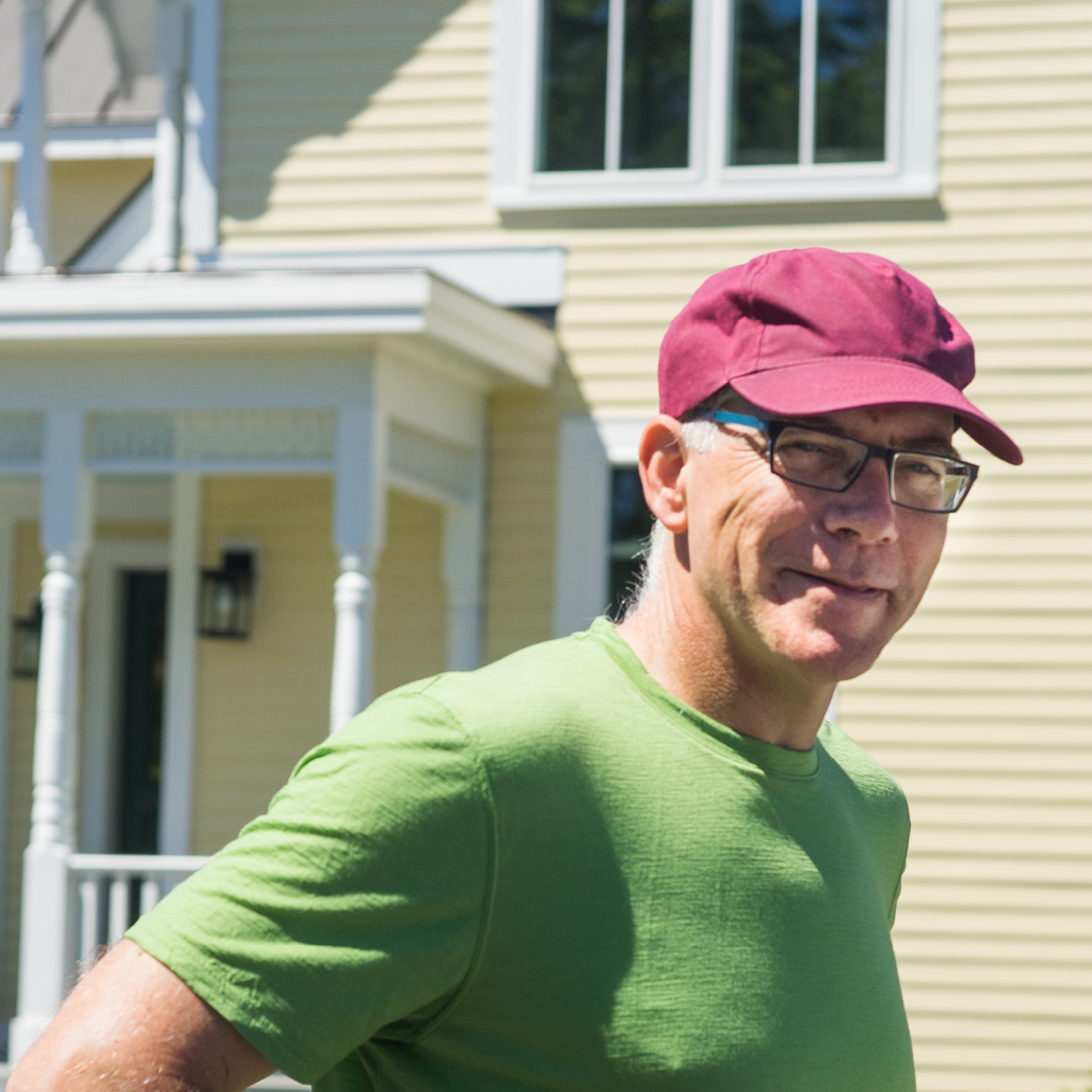 Middle aged man wearing red baseball cap and green T-shirt standing in front of yellow house