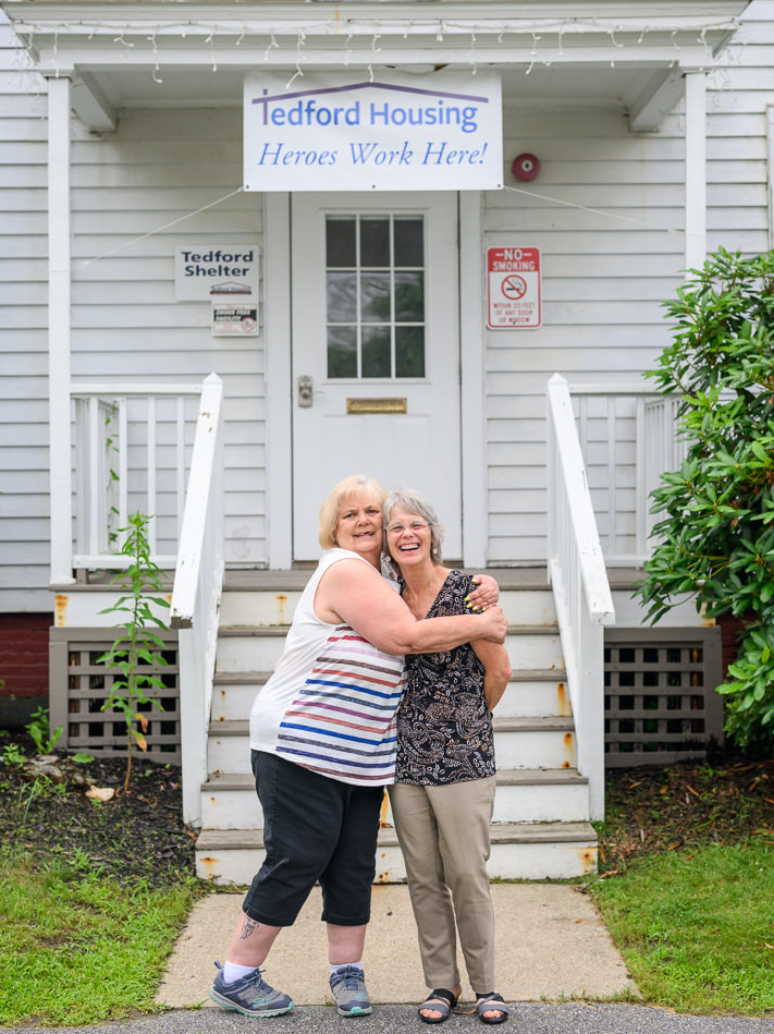 Two employees embrace and share a laugh in front of one of Tedford Housing's homeless shelters in Brunswick, Maine.