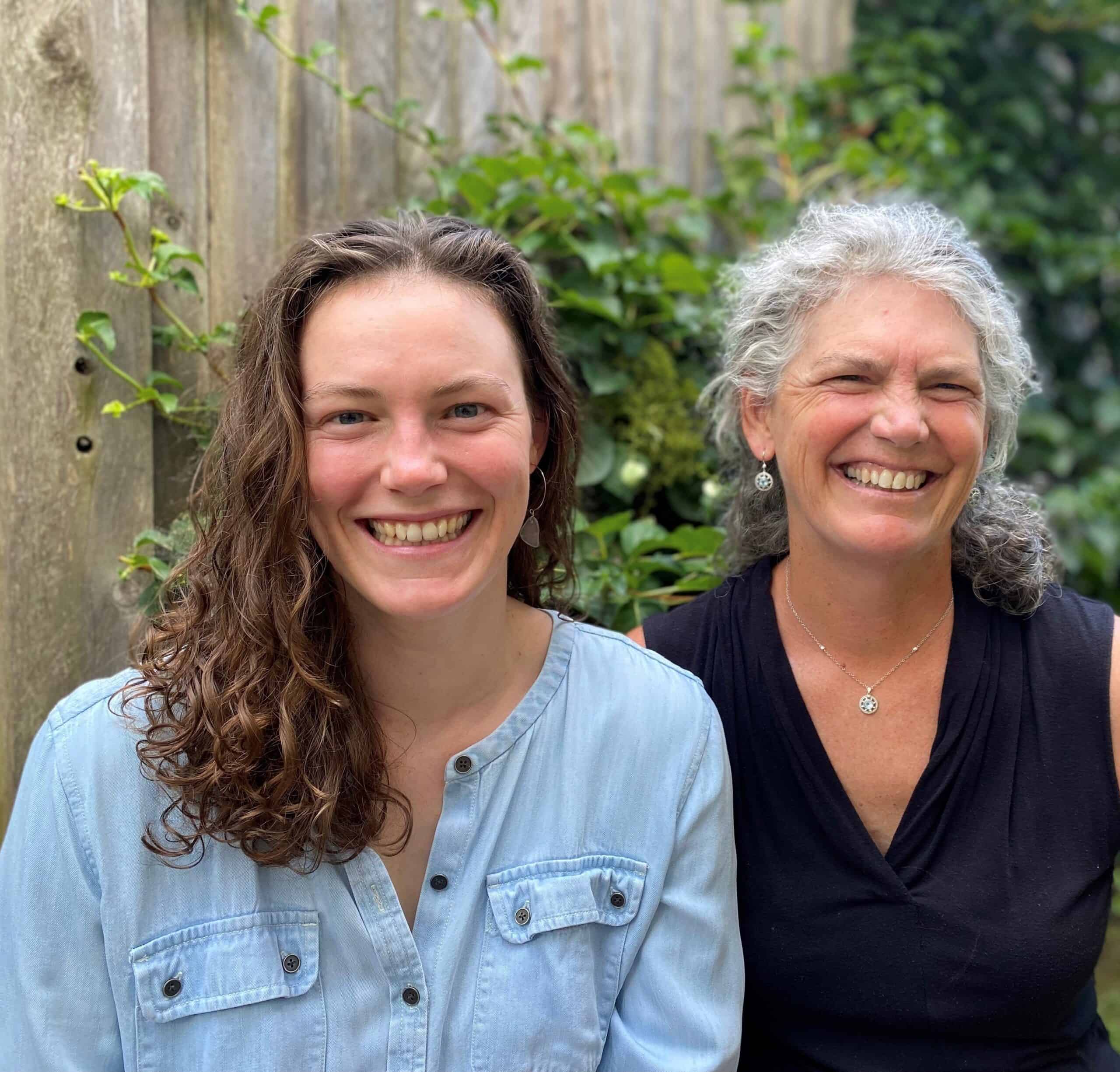 Young woman in blue shirt with her mother in purple shirt, both smiling