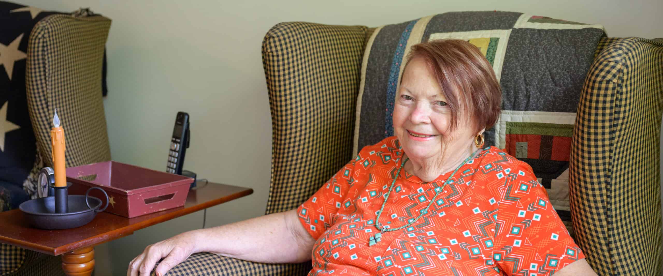 Elderly woman smiling on a cozy armchair in a home setting.