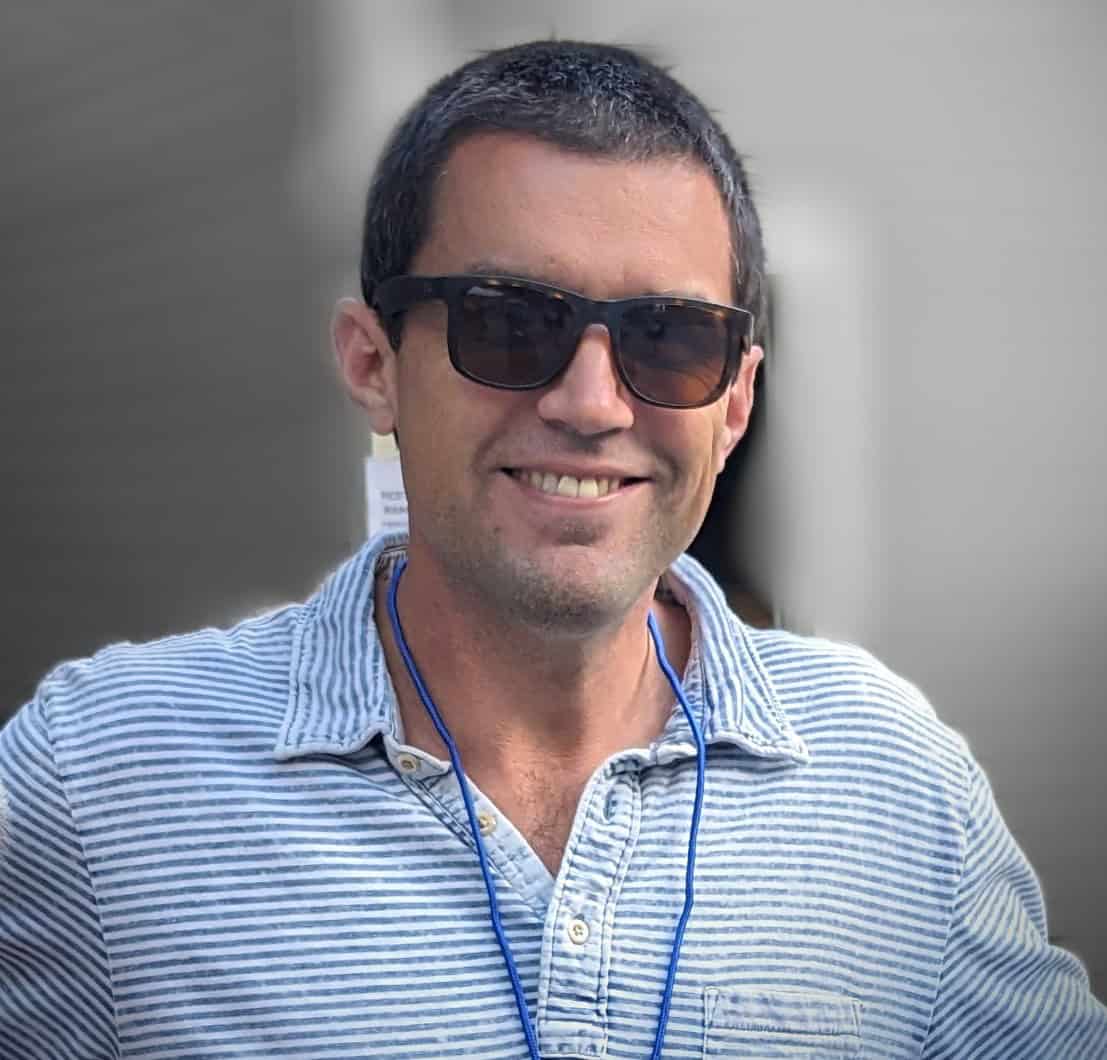 Smiling man wearing sunglasses and a striped shirt outdoors.