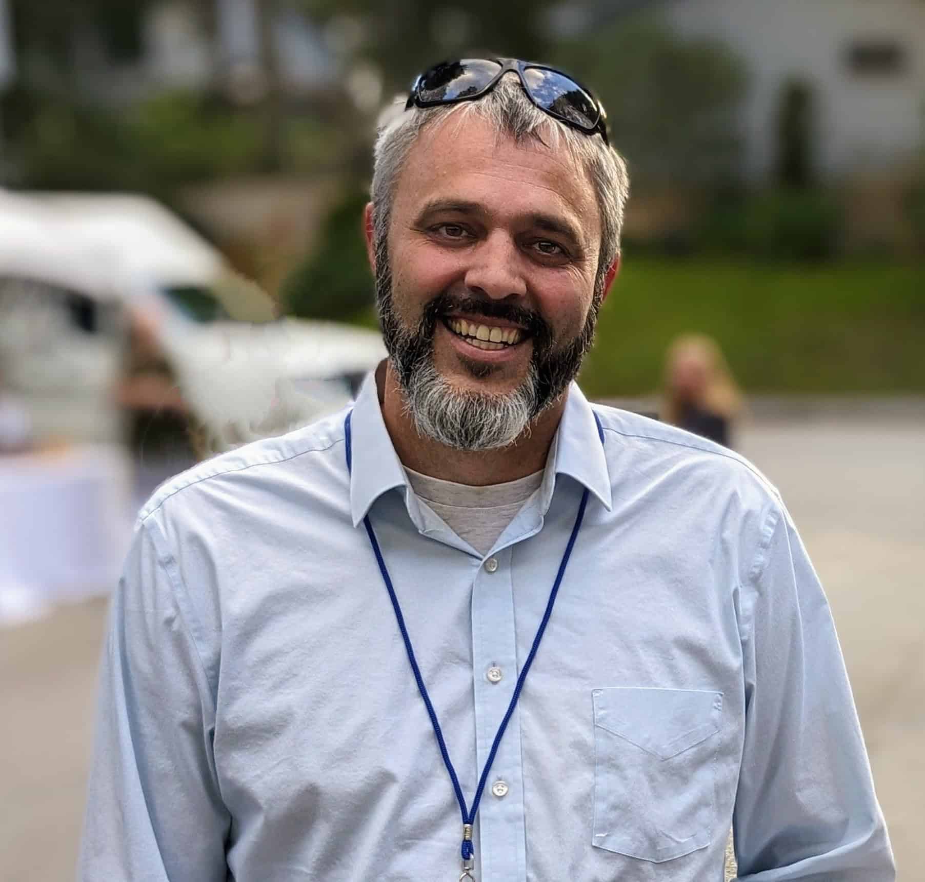 Smiling man with sunglasses on head at outdoor event.