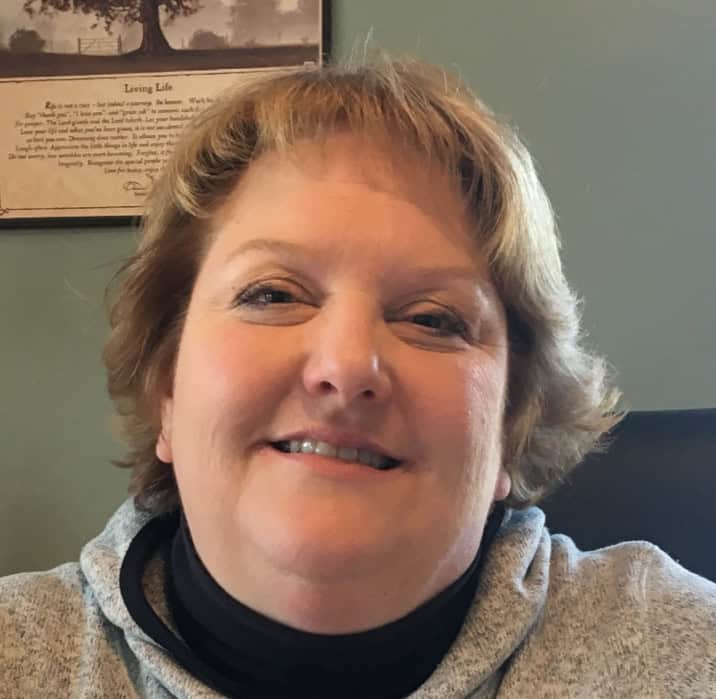Smiling woman with short blonde hair in a cozy indoor setting.