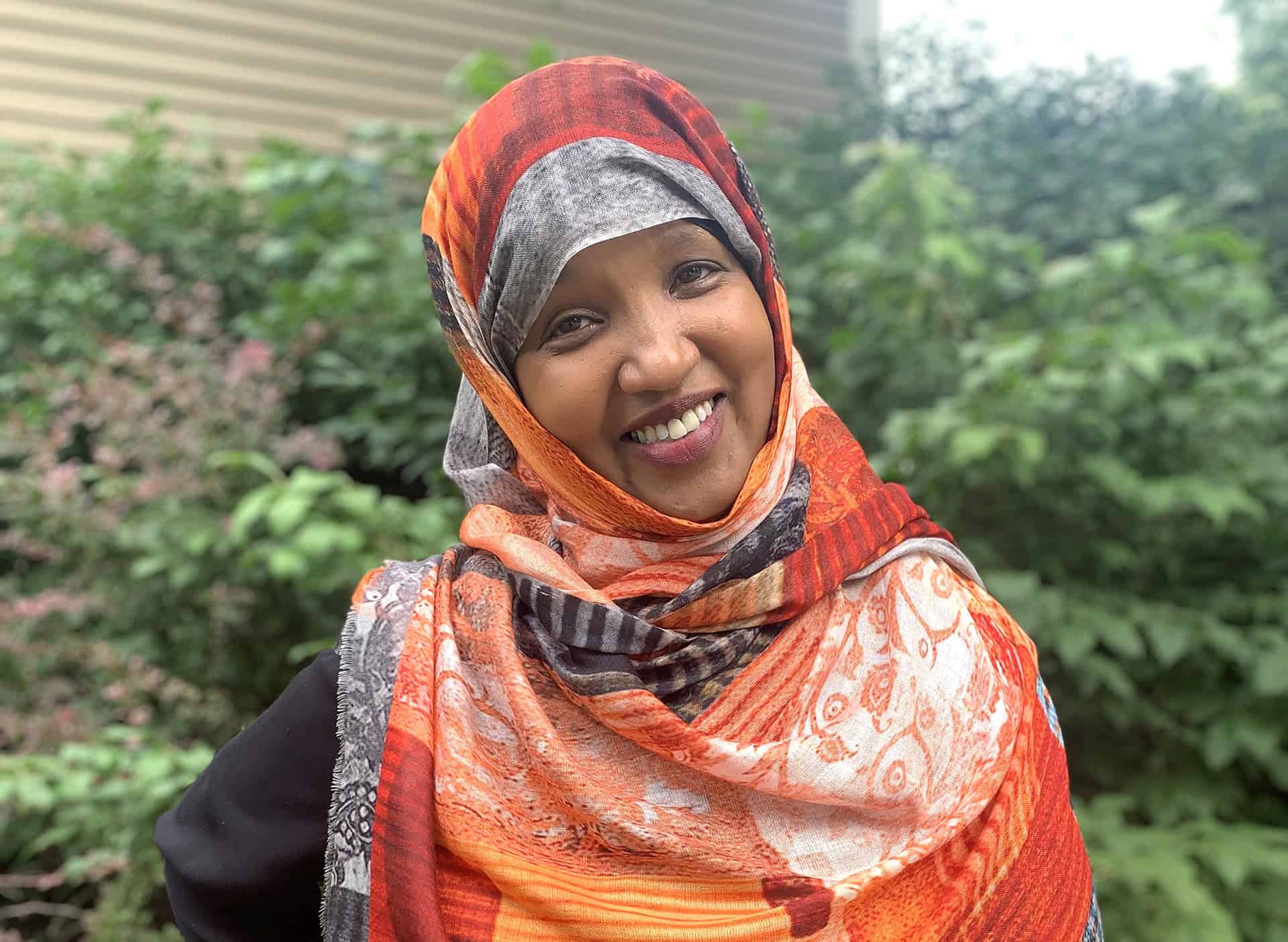 Smiling woman wearing a colorful headscarf outdoors.