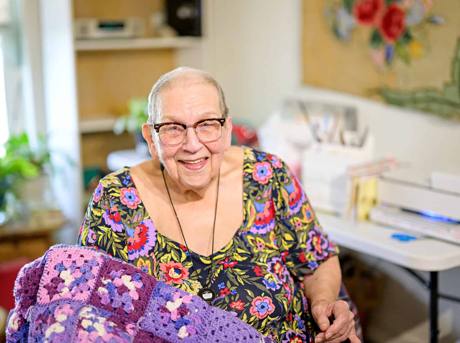 Elderly woman smiling with glasses in a cozy home setting.