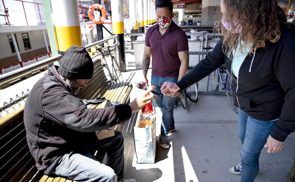 People helping homeless man on city street with donation and support.