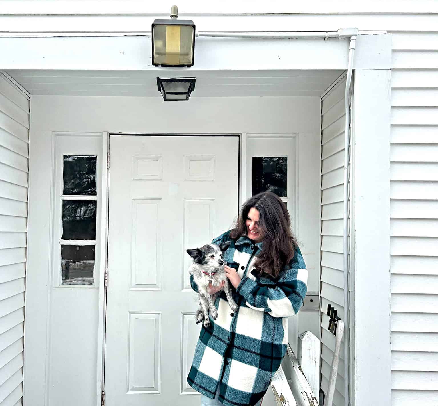 Woman holding a cat outside a house with white siding and a front door.
