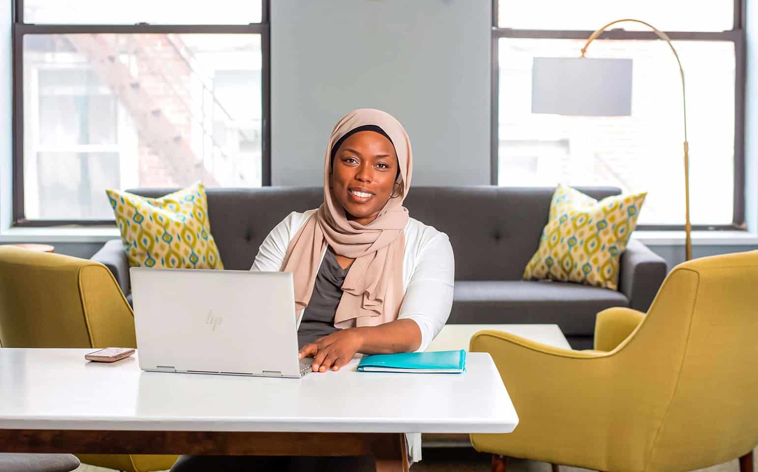 Woman in hijab working on laptop in modern office setting.