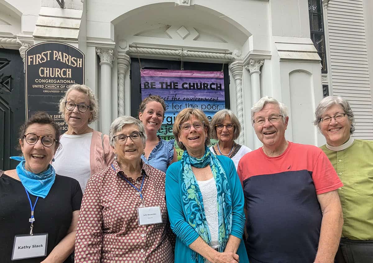 Group of diverse seniors smiling outside First Parish Church during community event.