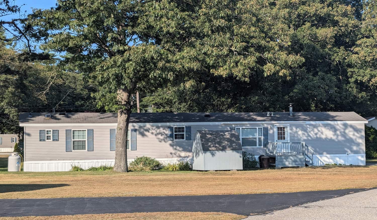 Mobile home in a community with trees and a clear sky.