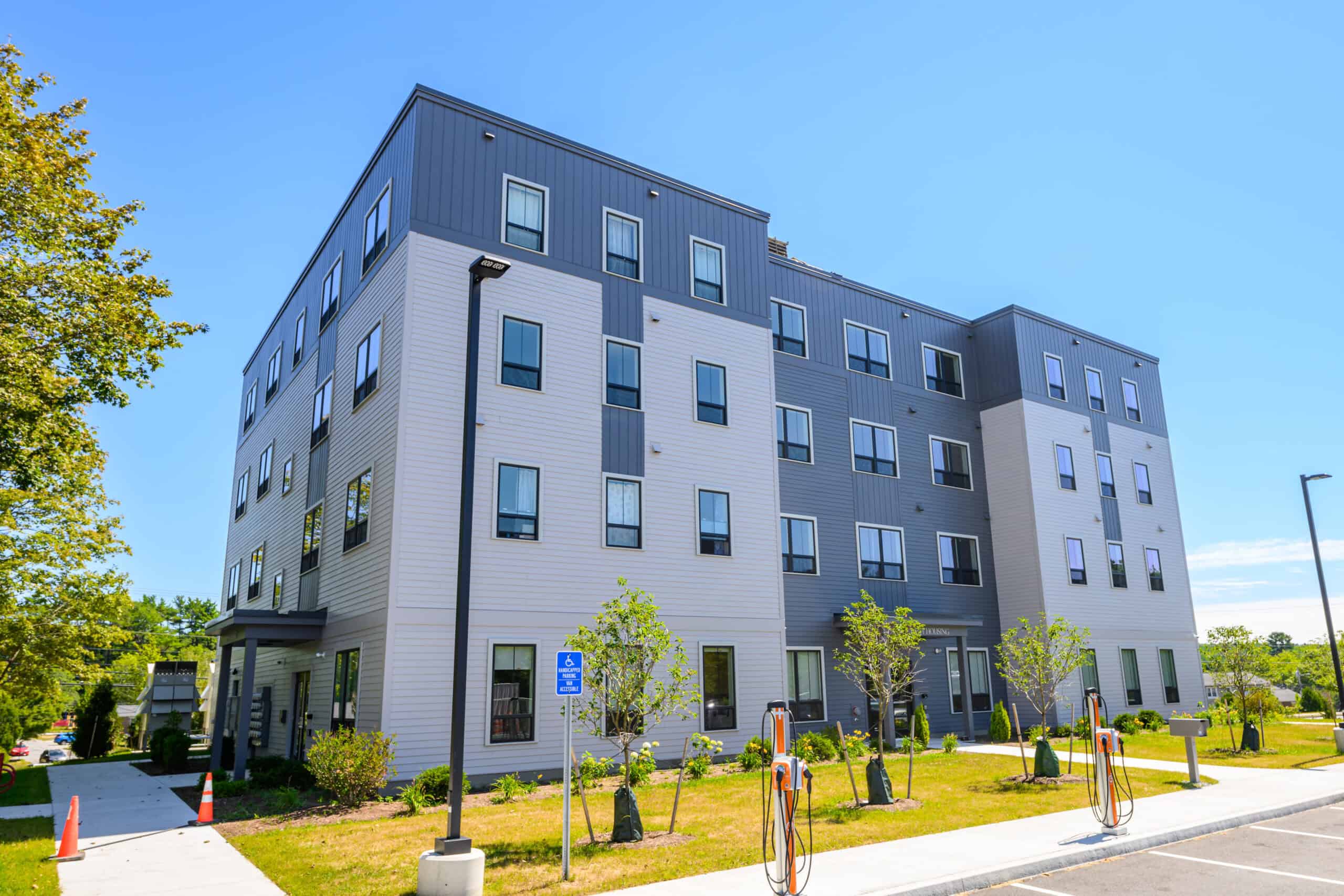 Modern multi-story apartment building with trees and parking area.