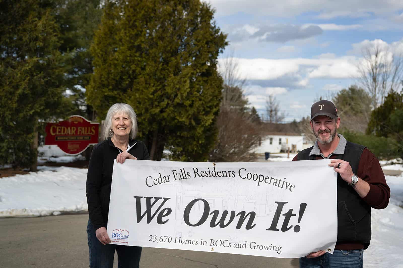 Cedar Falls residents holding a 'We Own It!' banner outdoors in winter.