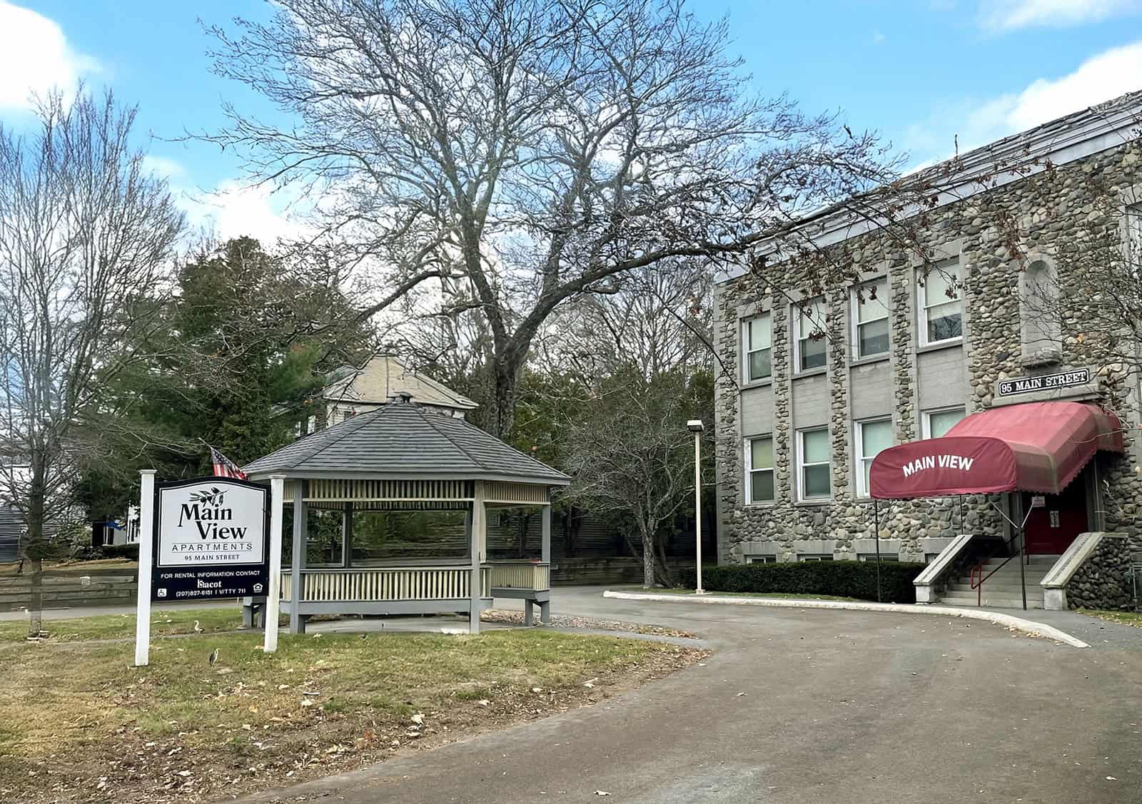 Main View Apartments building with a gazebo in front, trees, and clear sky.
